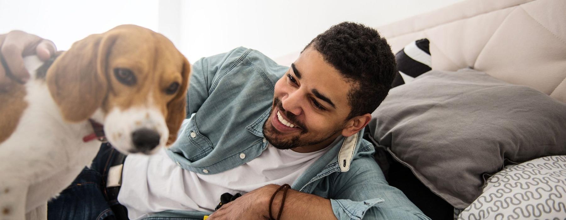 man smiles and pets his dog on a bed